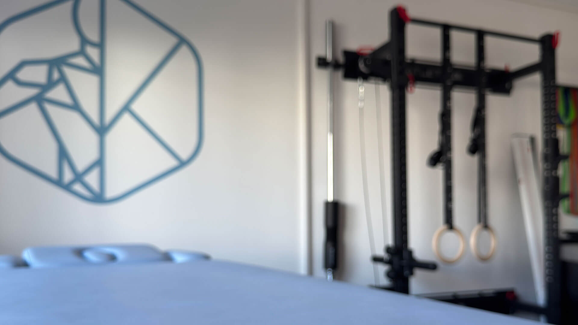 Blaue Behandlungsliege im Hintergrund eine Wand mit Fitnessgeräten für Physiotherapie.